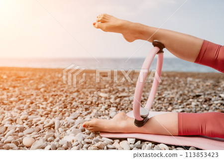 Woman sea pilates. Sporty happy middle aged woman practicing fitness on beach near sea, smiling active female training with ring on yoga mat outside, enjoying healthy lifestyle, harmony and meditation Woman sea pilates. Sporty happy middle aged woman practicing fitness on beach near sea, smiling active female training with ring on yoga mat outside, enjoying healthy lifestyle, harmony and meditation 113853423