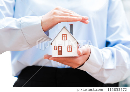 Hands holding a small house model, depicting safety and security in homeownership. Hands holding a small house model, depicting safety and security in homeownership. 113853572