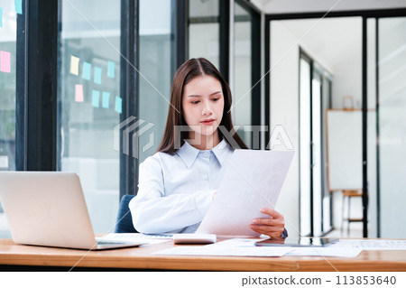 Focused Businesswoman Analyzing Document in Office Focused Businesswoman Analyzing Document in Office 113853640
