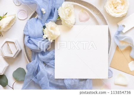 Card near blue tulle fabric knot and cream roses on plates top view copy space, wedding mockup Card near blue tulle fabric knot and cream roses on plates top view copy space, wedding mockup 113854736