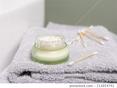 Opened green cream jar on grey folded bath towel close up,  cosmetic skincare product 113854742