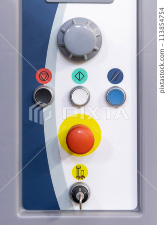 Grey control panel with big red button and other buttons and switches for machinery operation in production 113854754