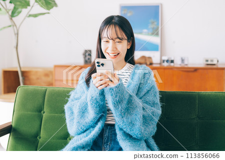 Woman using smartphone on sofa 113856066