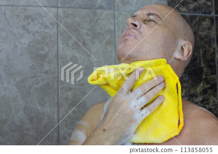 Bald man in shower washing his head with washcloth Bald man in shower washing his head with washcloth 113858055