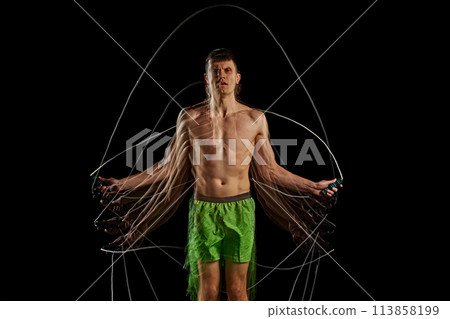 Passion and determination to fitness. Athletic man wit shirt6less muscular body training, jumping rope against black background with stroboscope effect 113858199