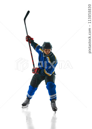 Ready to attack, athletic hockey player, geared up and focused, glides with stick held high against white studio background. 113858830