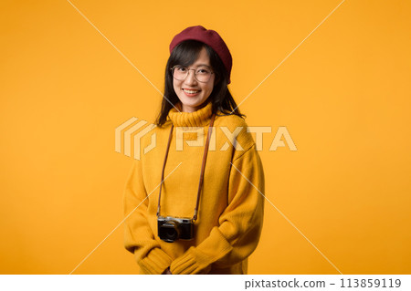 A creative artist, this young Asian woman, dressed in a yellow sweater and red beret, captures moments with her camera, a delightful hobby. 113859119