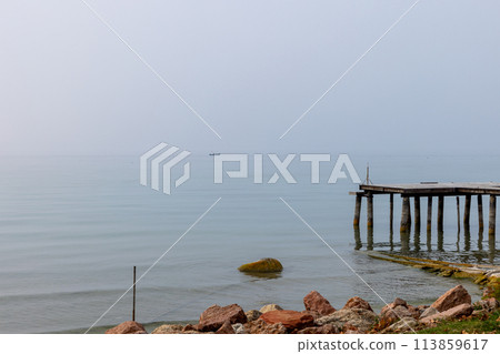 Old pier on Lake Garda with a boat in the distant fog 113859617