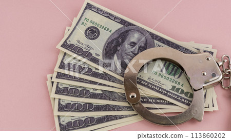 iron handcuffs and hundred dollar bills on a pink background iron handcuffs and hundred dollar bills on a pink background 113860202