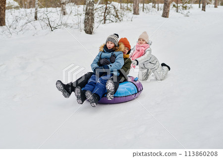 Girl pushing snow tube with friends 113860208