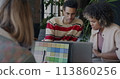 African American businessman talking to female colleague while lady designer working with laptop in creative office. Start-up and coworking concept. 113860256