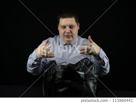 Male businessman folds stacks of hundred dollar bills into a large bag on a black background. A man collects money in a bag on the table. Concept money, million, wealth, dollars. 113860441