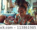 happy dark-skinned woman drawing with pencils in colouring book 113861985