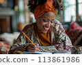 happy dark-skinned woman drawing with pencils in colouring book 113861986