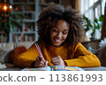 happy dark-skinned woman drawing with pencils in colouring book 113861993
