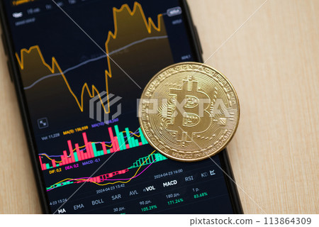 Bitcoin coin on the background of a smartphone screen with a graph of fall of cryptocurrency market on the exchange. Bear market, dump, losses concept. Bitcoin coin on the background of a smartphone screen with a graph of fall of cryptocurrency market on the exchange. Bear market, dump, losses concept. 113864309