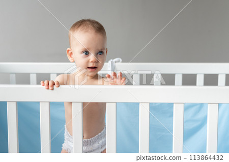 Interested baby leaning on the back of a wooden crib Interested baby leaning on the back of a wooden crib 113864432