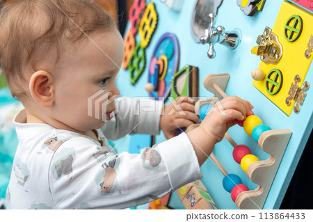 Close-up of a cute toddler playing with wooden elements on a busy board Close-up of a cute toddler playing with wooden elements on a busy board 113864433