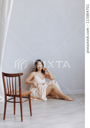 A woman is sitting on a wooden chair in a room with white walls A woman is sitting on a wooden chair in a room with white walls 113864701