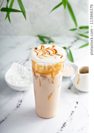 Caramel milk tea latte in a tall glass with cold foam and caramel sauce 113866376