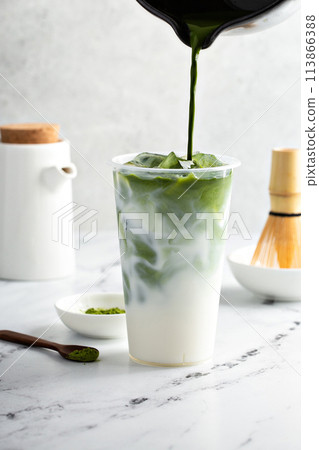 Making iced matcha latte in a tall glass with ice by adding matcha tea to milk Making iced matcha latte in a tall glass with ice by adding matcha tea to milk 113866388