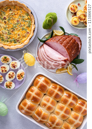 Easter brunch on large table with spiral sliced ham, quiche, deviled eggs and hot cross buns Easter brunch on large table with spiral sliced ham, quiche, deviled eggs and hot cross buns 113866527