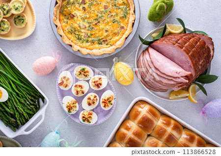 Easter brunch on large table with spiral sliced ham, quiche, deviled eggs and hot cross buns Easter brunch on large table with spiral sliced ham, quiche, deviled eggs and hot cross buns 113866528