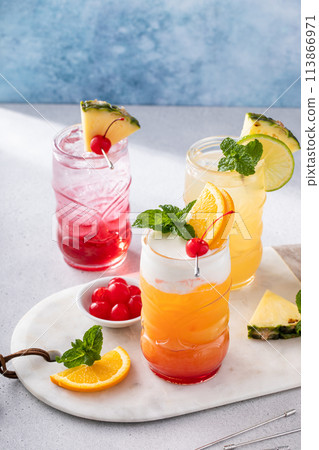 Variety of tropical tiki cocktails in fun tiki glasses garnished with slices of fruit and mint 113866971