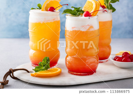 Tropical tiki cocktail with cold foam, garnished with orange slices, cherry and mint 113866975