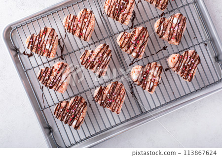 Pink heart shaped rice krispie treats drizzled with dark chocolate on a cooling rack 113867624