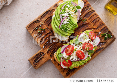 Avocado toasts with radishes, tomatoes and feta topped with olive oil 113867740