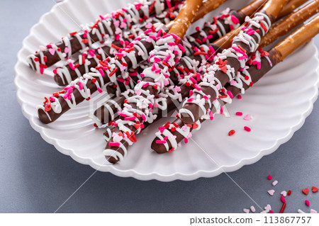 Chocolate dipped pretzel rods with pink heart sprinkles on a plate Chocolate dipped pretzel rods with pink heart sprinkles on a plate 113867757