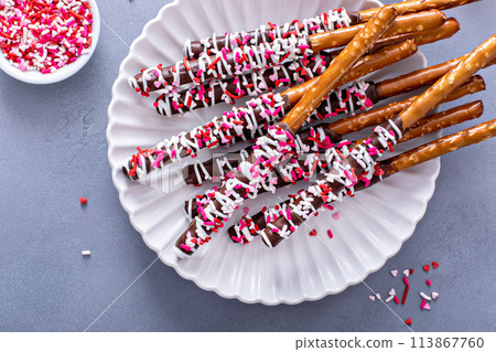 Chocolate dipped pretzel rods with pink heart sprinkles on a plate 113867760