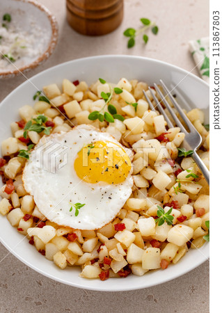 Potato hash with bacon or prosciutto served with fried egg on top 113867803