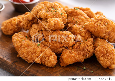 Chicken nuggets or chicken strips on a board with dipping sauces, fries and celery 113867819