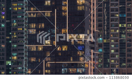 Rows of glowing windows with people in apartment building at night. Rows of glowing windows with people in apartment building at night. 113868030