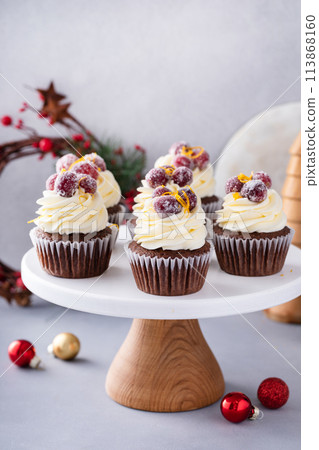 Festive chocolate and orange cupcakes with white chocolate frosting garnished with sugared cranberry 113868160