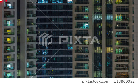 Rows of glowing windows with people in apartment building at night. 113869052