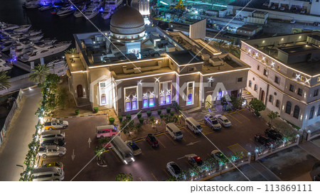 Yachts in Dubai Marina flanked by the Al Rahim Mosque and residential towers and skyscrapers aerial night to day timelapse. 113869111