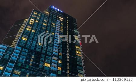 Night Sky with clouds above modern skyscraper with glowing windows architecture timelapse. Night Sky with clouds above modern skyscraper with glowing windows architecture timelapse. 113869153