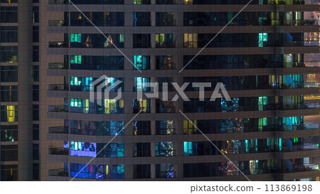 Rows of glowing windows with people in apartment building at night. 113869198