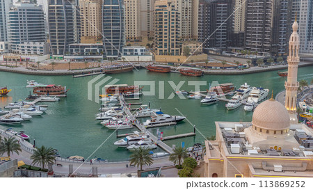 Yachts in Dubai Marina flanked by the Al Rahim Mosque and residential towers and skyscrapers aerial day to night timelapse. 113869252