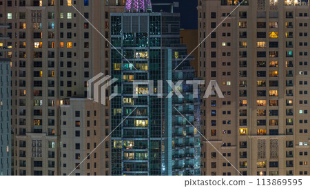 Glowing windows in multistory modern glass residential building light up at night timelapse. Glowing windows in multistory modern glass residential building light up at night timelapse. 113869595