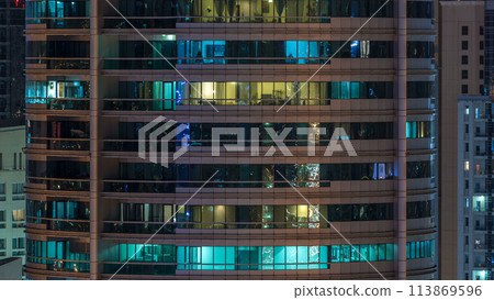 Glowing windows in multistory modern glass residential building light up at night timelapse. 113869596