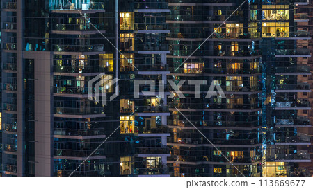 Glowing windows in multistory modern glass residential building light up at night timelapse. 113869677