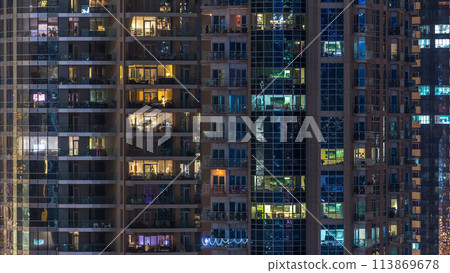 Glowing windows in multistory modern glass residential building light up at night timelapse. Glowing windows in multistory modern glass residential building light up at night timelapse. 113869678