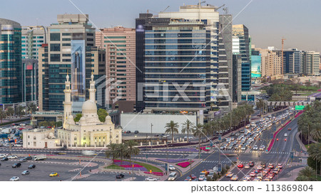 Mosque near Dubai Creek surrounded by modern buildings and busy traffic street day to night timelapse 113869804