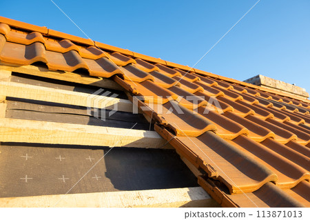 Overlapping rows of yellow ceramic roofing tiles mounted on wooden boards covering residential building roof under construction. 113871013