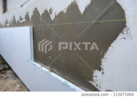Installation of styrofoam insulation sheets on house facade wall for thermal protection. 113871068