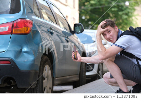 Sad male driver photographing on sellphone camera dented vehicle on street side for insurance service after car accident. Road safety concept Sad male driver photographing on sellphone camera dented vehicle on street side for insurance service after car accident. Road safety concept 113871092